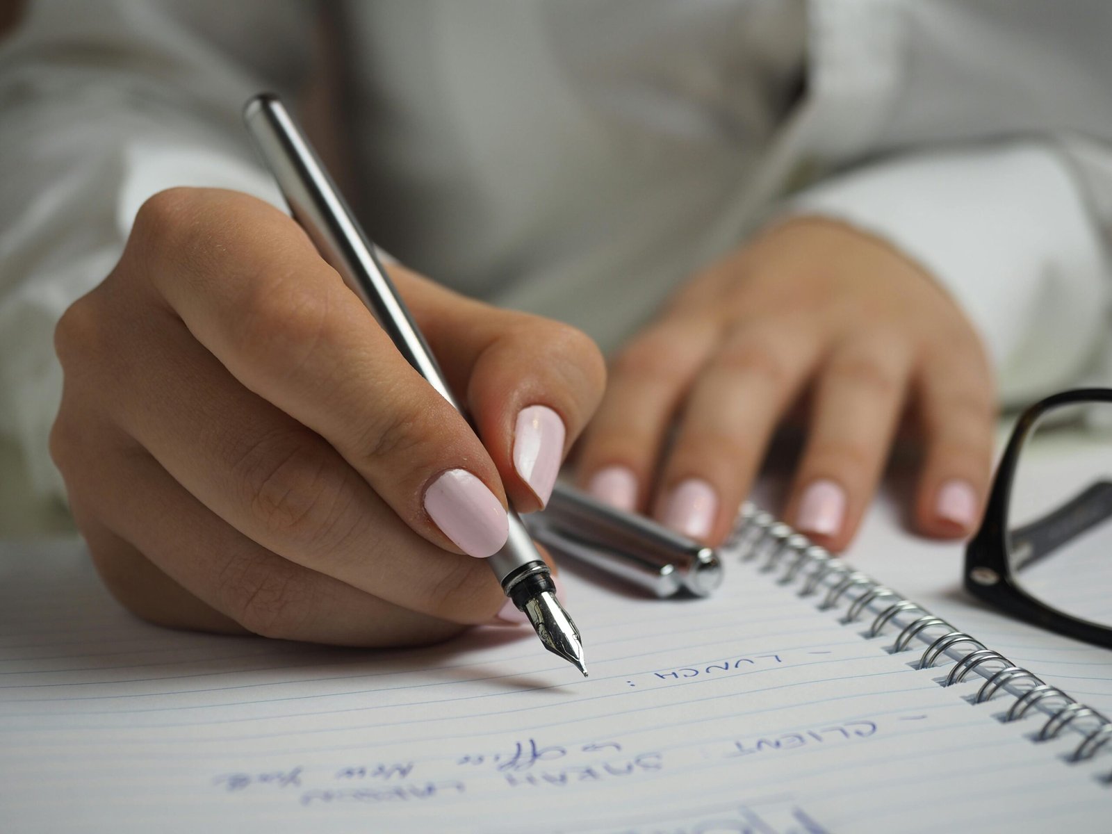 A detailed image of handwriting in a notebook with a fountain pen and glasses, ideal for office themes.